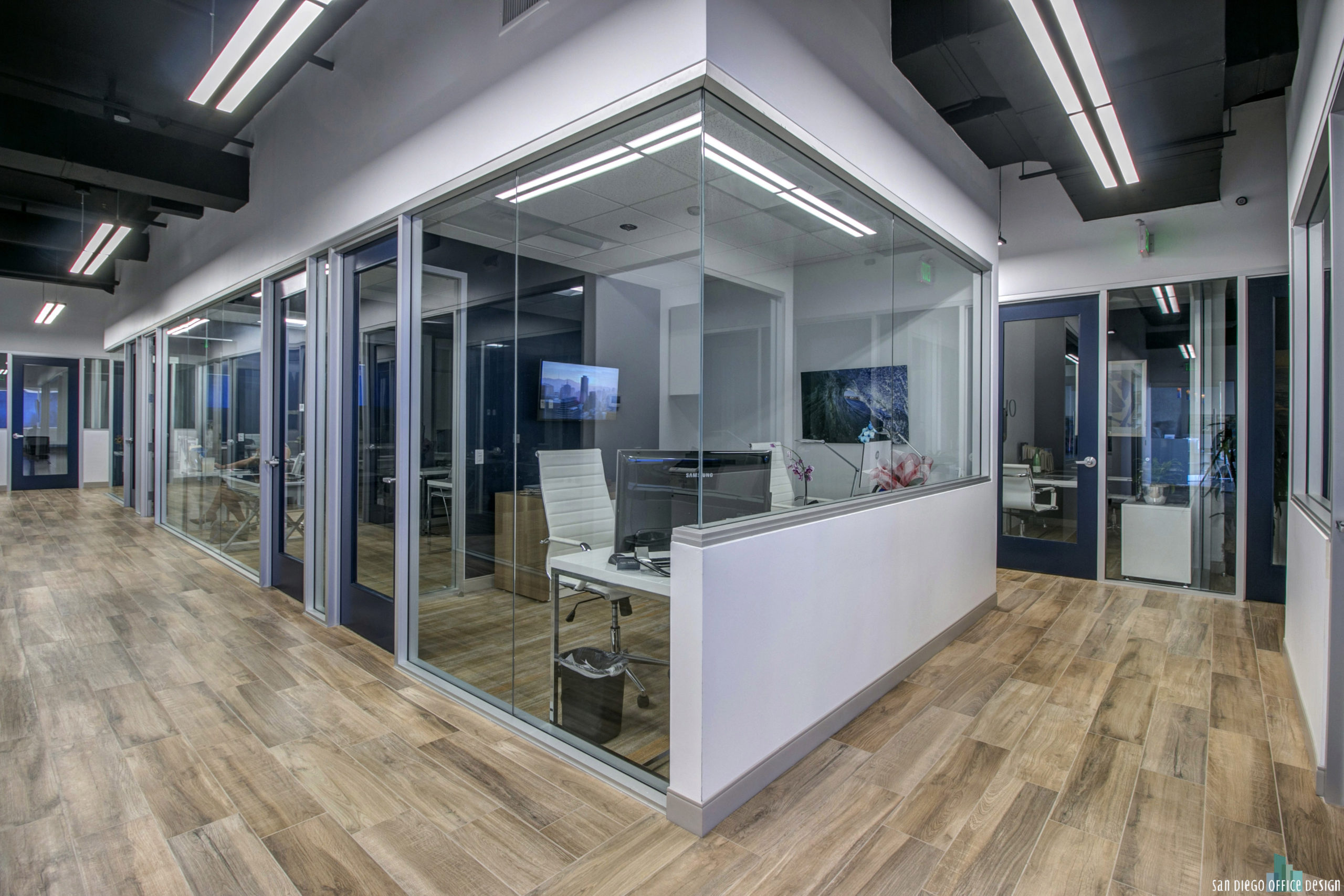 A row of offices with glass wall partitions, wood floors, and clean white walls between them