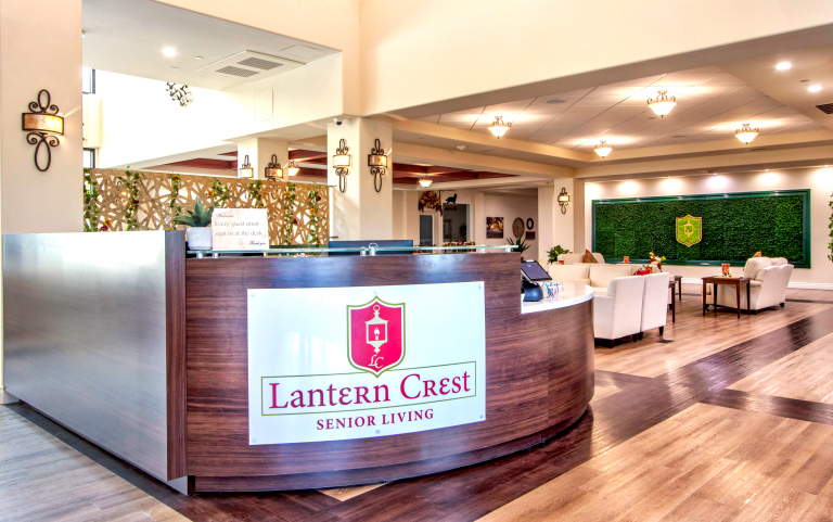 A large wraparound desk that reads "Lantern Crest Senior Living" with seating and a moss wall to the left